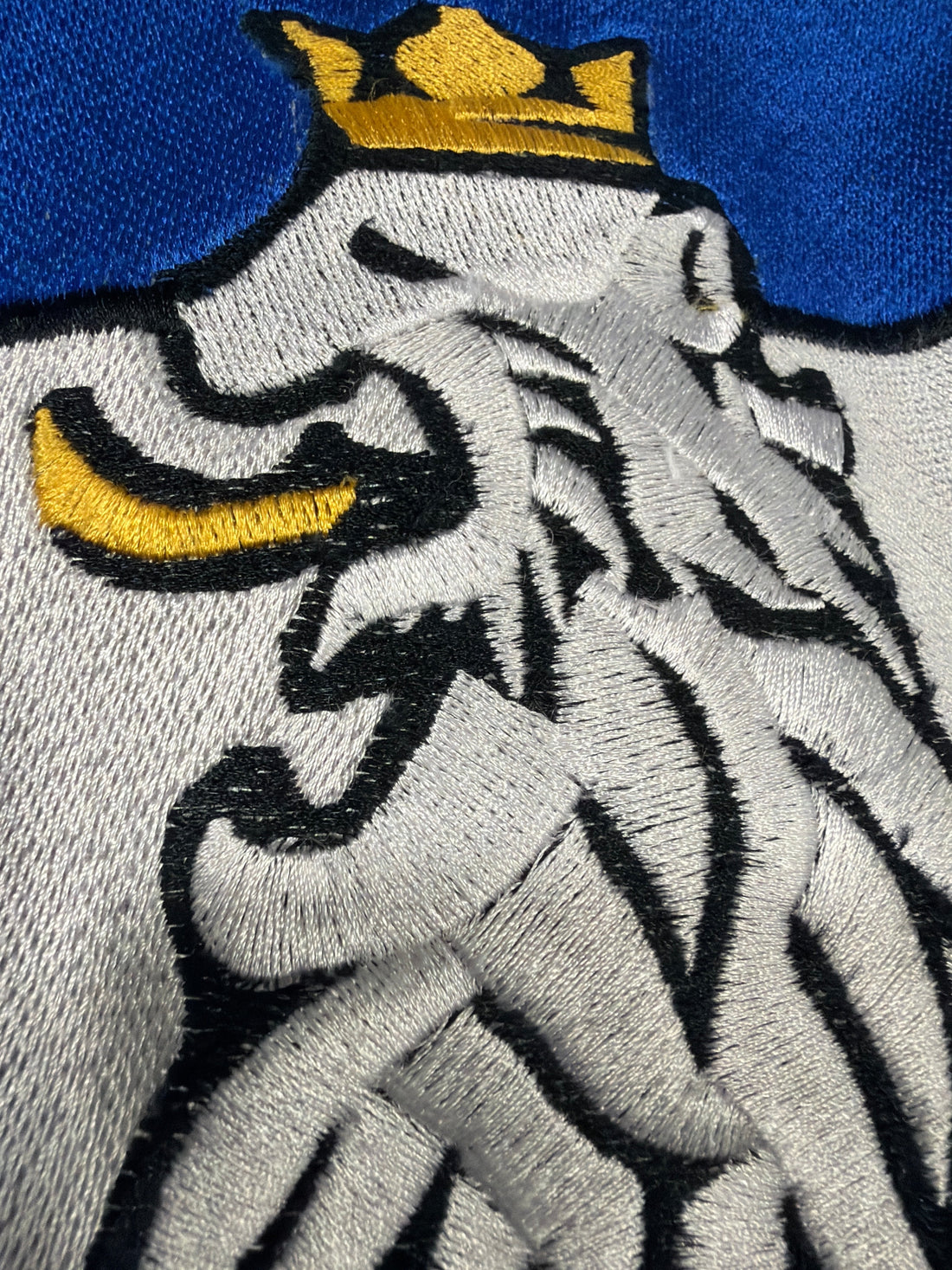 Macro close-up of R10’s lion embroidery featuring gold crown and fine stitching, symbolizing luxury craftsmanship, precision, and timeless quality.
