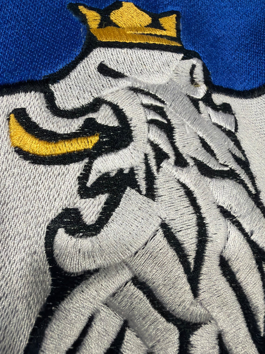 Macro close-up of R10’s lion embroidery featuring gold crown and fine stitching, symbolizing luxury craftsmanship, precision, and timeless quality.