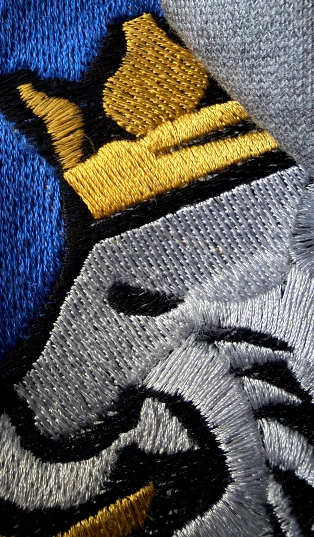 Close-up detail of the Royalty10 embroidered lion emblem in gold, blue, grey, and black threadwork — a symbol of craftsmanship, refinement, and disciplined design.