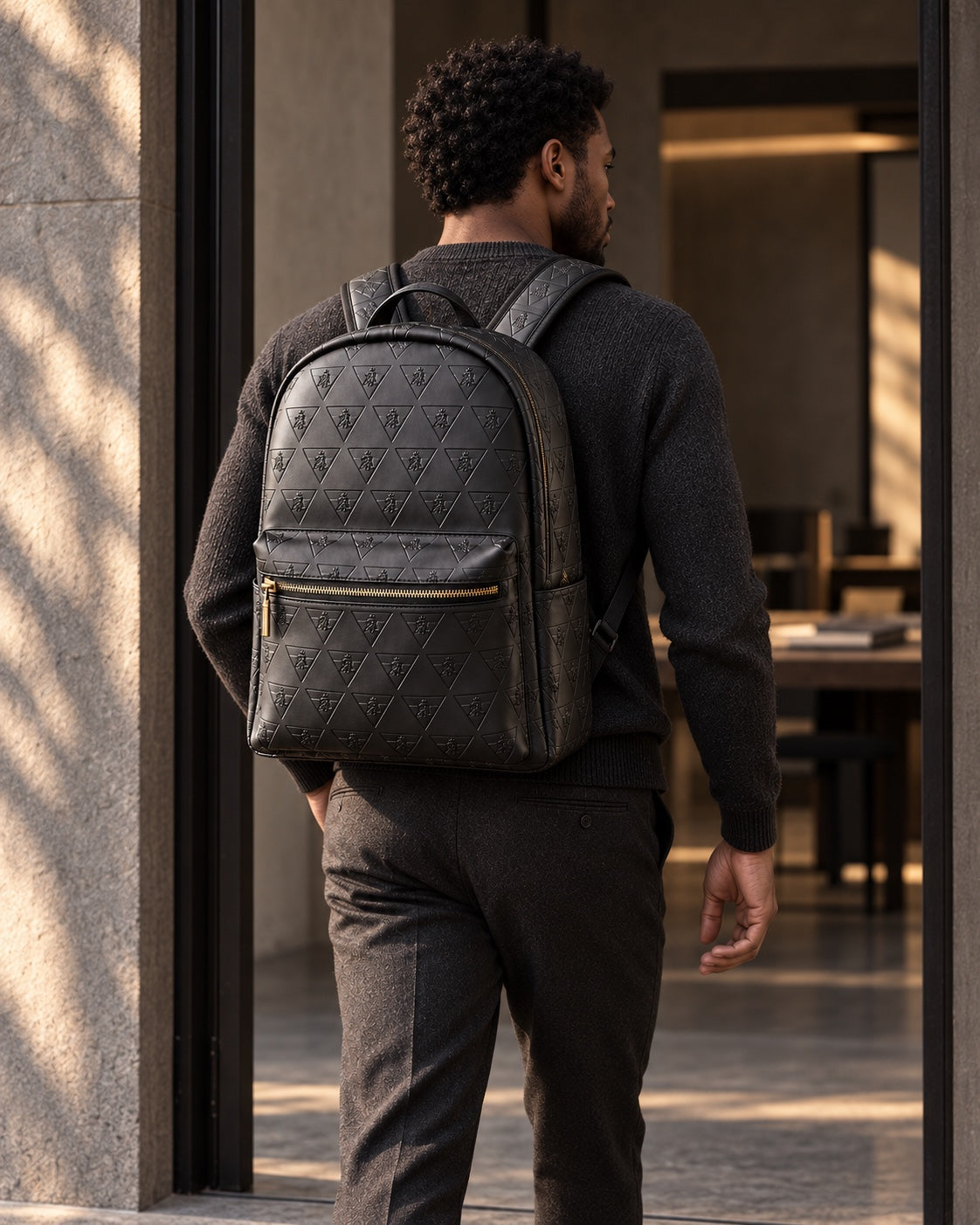 A man wearing the R10 backpack enters a quiet workspace through a shaded doorway.