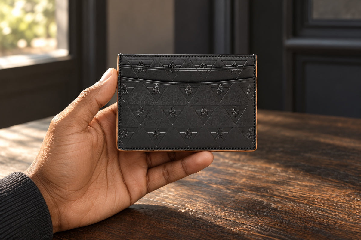 A hand holds the black R10 Leão Branco cardholder above a wooden table beside a window.