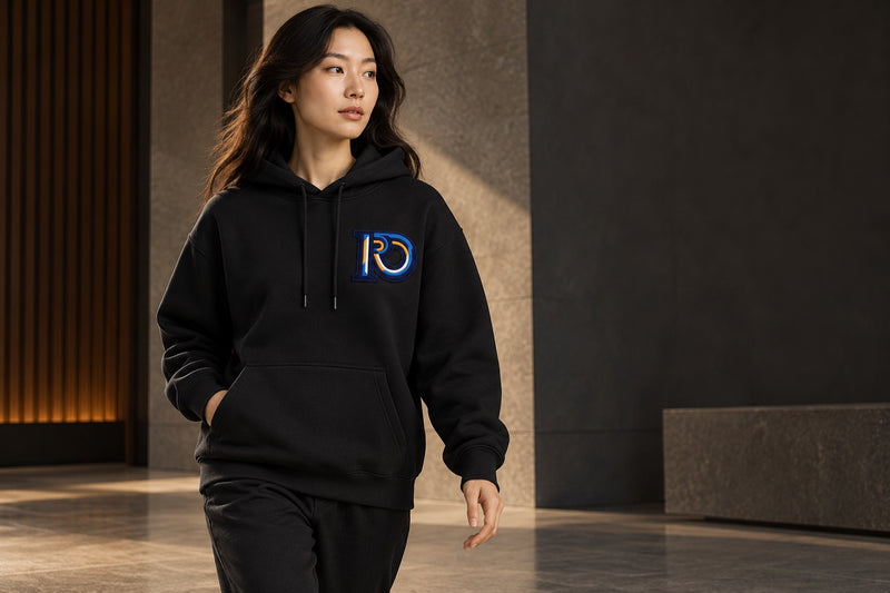Model wearing an R10 heavyweight black hoodie in a quiet architectural interior.