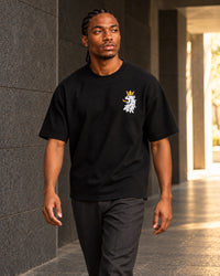 Black R10 Leão Branco Motif Tee — worn walking through a stone passage.