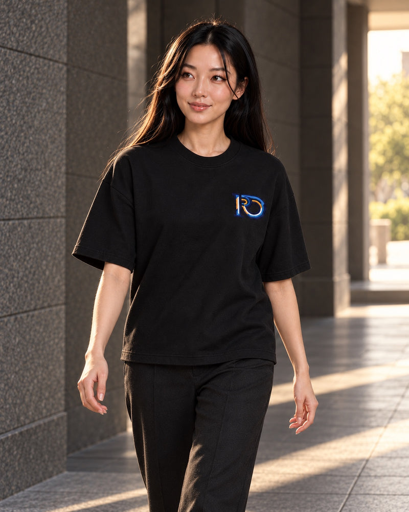 Black R10 Monogram Tee — worn walking through a stone passage.