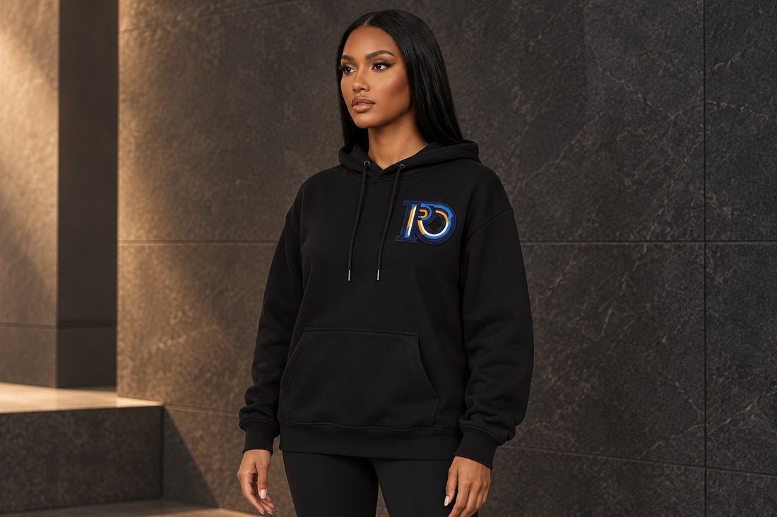 Model wearing a black R10 Monogram pullover hoodie with its drawcord, pocket, cuffs, and hem visible.