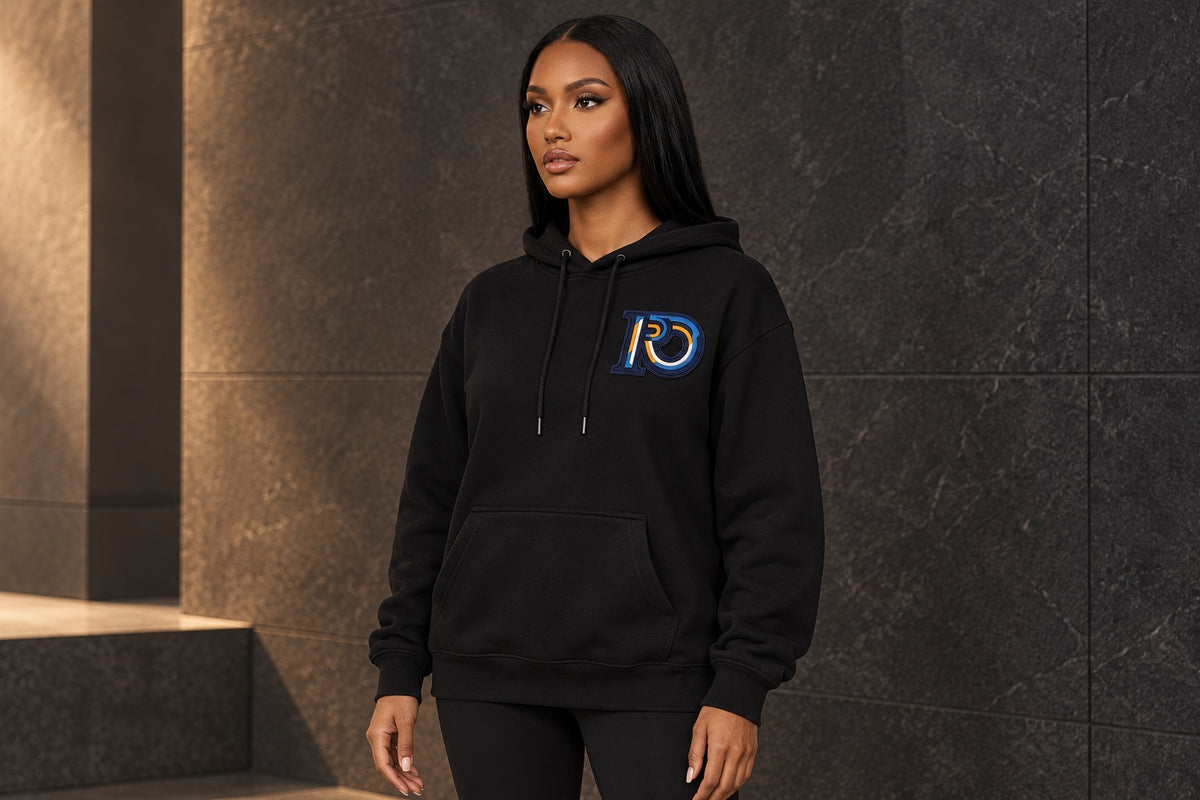 Model wearing a black R10 Monogram pullover hoodie with its drawcord, pocket, cuffs, and hem visible.