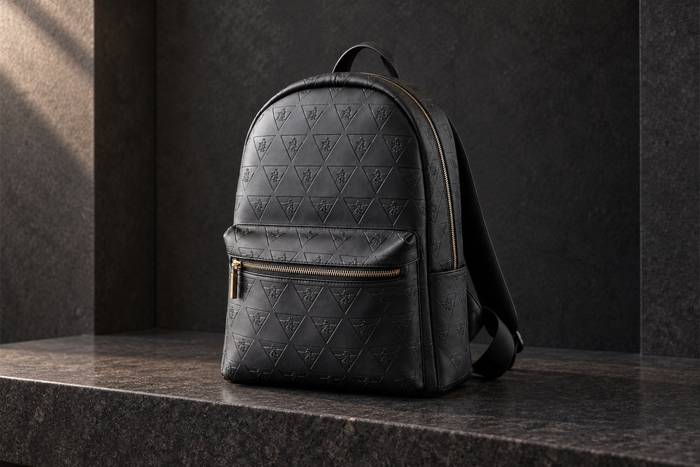Black R10 Leão Branco backpack standing on a stone bench, showing its complete silhouette, front pocket, and gold-tone zippers.