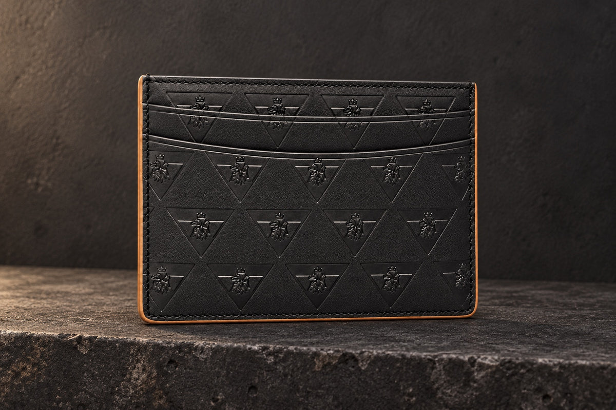 Black R10 Leão Branco cardholder on a stone ledge, showing its front slots, embossed motif, and stitched perimeter.
