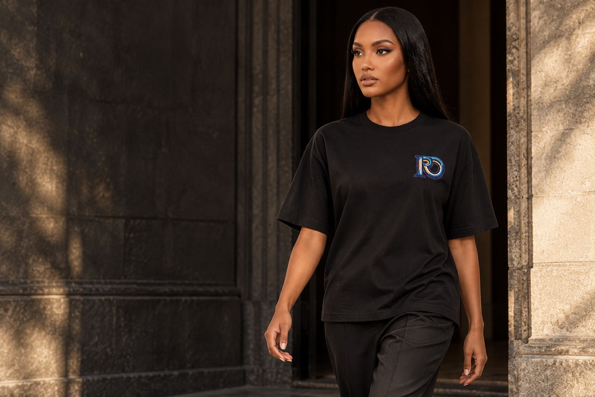 Model wearing the black R10 Monogram Tee beside a stone doorway.