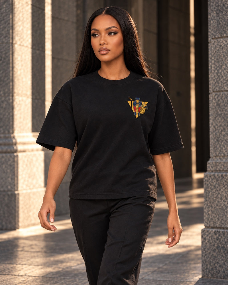 Black R10 Uraeus e Abutre Emblem Tee — worn walking through a stone passage.