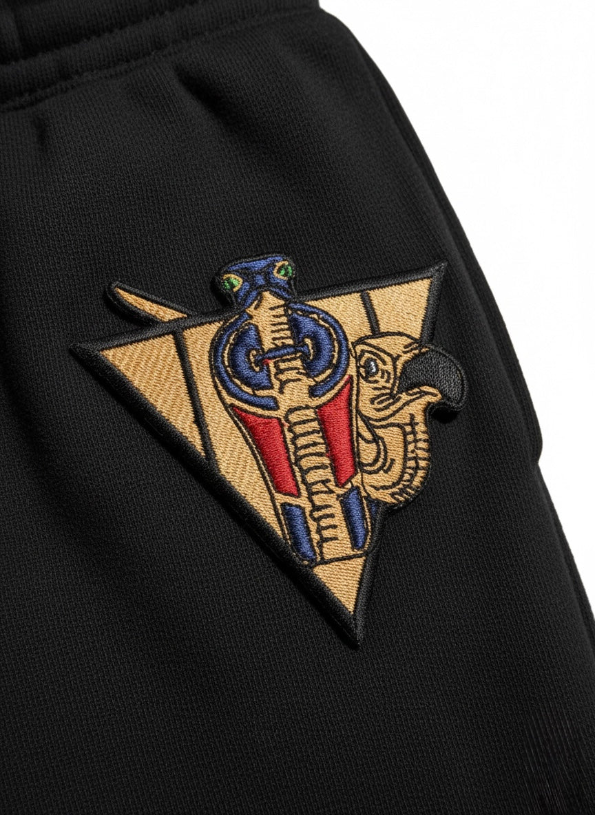 Detail view of embroidered cobra and vulture emblem on R10 Uraeus e Abutre joggers.